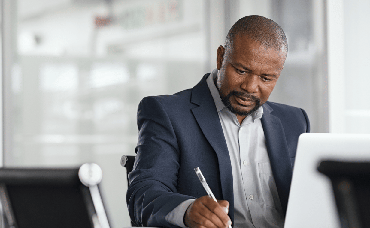 A professional man writing with a pen on paper in an office setting, capturing a thoughtful moment of work and focus